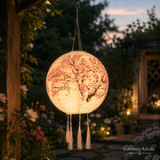 Solar-Lampion mit Kirschblütenmotiv und Quasten, beleuchtet auf einer Gartenterrasse in der Abenddämmerung