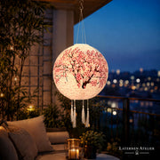 Runder Solar-Lampion mit Kirschblütenmotiv, hängend auf einer Terrasse mit Stadtblick bei Nacht