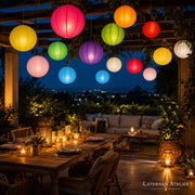 Bunte Papierlampions hängend über einer Terrasse in der Abenddämmerung mit Lichterkette