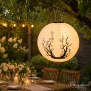 Runder Solar-Lampion mit Kirschblütenmotiv, hängend über einem gedeckten Gartentisch am Abend