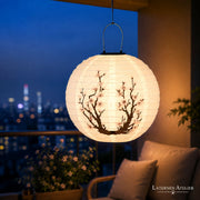 Runder Solar-Lampion mit Kirschblütenmotiv, hängend auf einem Balkon mit Skyline-Blick bei Nacht