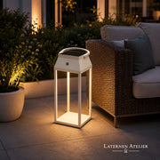 Akku-Solar-Laterne mit warmem Licht neben Outdoor-Lounge im Garten