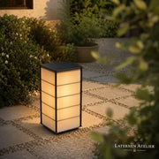 Japanische Solar-Laterne mit warmem Licht auf einem Gartenweg zwischen Pflanzen