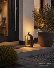 Schwarze Metalllaterne mit warmem LED-Licht am Hauseingang neben einer Pflanze