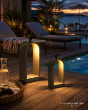 Zwei schwarze Metalllaternen mit warmem Licht auf einer Terrasse am Pool bei Abendstimmung