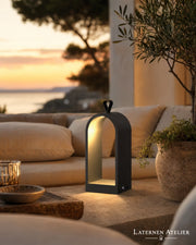 Schwarze Metalllaterne mit warmem Licht auf einer Terrasse neben einem Sofa bei Sonnenuntergang