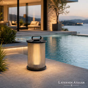 Schwarze Outdoor Solar-Laterne mit warmem Licht auf einer modernen Terrasse am Pool
