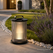 Schwarze Outdoor Solar-Laterne mit warmem LED-Licht neben Pflanzen und Gartenweg