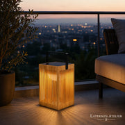 Kompakte Solar-Laterne aus Bambus mit warmem LED-Licht auf einem Balkon neben einer Outdoor-Lounge
