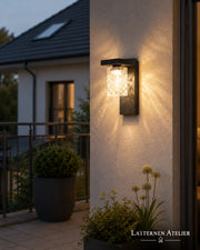 Solar-Wandlaterne außen mit warmem Licht an einer Balkonwand mit Pflanzen