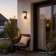 Solar-Wandlaterne außen mit warmem Licht neben einem Sitzbereich auf der Terrasse