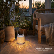 Weiße Solar-Laterne mit warmem Licht neben einem Sitzbereich auf der Terrasse