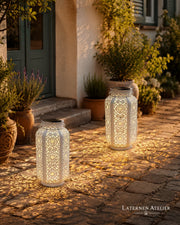 Weiße Laterne mit dekorativem Lichtmuster auf einem Gartenweg im Außenbereich