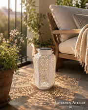 Weiße Solar-Laterne mit warmem Licht auf einem Balkon neben einem Sitzbereich