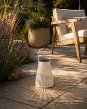 Weißes Solar-Windlicht mit Lichtmuster auf einer Terrasse neben Gartenmöbeln