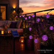 Lila Solar-Lampion-Lichterkette mit Solarpanel auf dem Balkon bei Sonnenuntergang