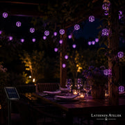 Lila Solar-Lampion-Lichterkette beleuchtet einen gedeckten Gartentisch am Abend