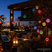 Bunte Solar-Lampion-Lichterkette beleuchtet eine Dachterrasse bei Nacht mit Stadtblick